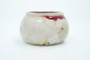 Off white ceramic pot with red spotches and a small gold peace symbol drawing.