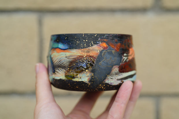 Ceramic pot with many colors and shining elements, looking like an abstract desert landscape.