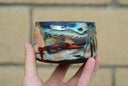 Ceramic pot with many colors and shining elements, looking like an abstract desert landscape.