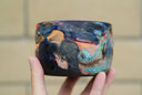 Ceramic pot with many colors and shining elements, looking like an abstract desert landscape.