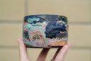 Ceramic pot with many colors and shining elements, looking like an abstract desert landscape.