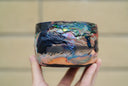 Ceramic pot with many colors and shining elements, looking like an abstract desert landscape.