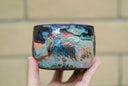 Ceramic pot with many colors and shining elements, looking like an abstract desert landscape.