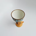 Ceramic green and blue striped cup with a brown floppy eared dog as a handle. Seen from overhead.