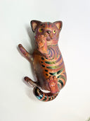 Ceramic cat figurine, reddish brown in color with chromatic stripes. It lays on its back in a playful position.
