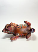 Ceramic cat figurine, reddish brown in color with chromatic stripes. It lays on its back in a playful position.