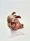 Ceramic cat figurine, reddish brown in color with chromatic stripes. It lays on its back in a playful position.