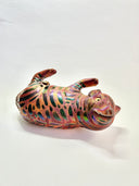 Ceramic cat figurine, reddish brown in color with chromatic stripes. It lays on its back in a playful position.