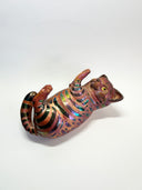 Ceramic cat figurine, reddish brown in color with chromatic stripes. It lays on its back in a playful position.