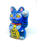 A hand-painted blue maneki-neko lucky cat figurine with black stripes, yellow eyes, pink inner ears, and a red collar, holding a yellow sign with black kanji characters, set against a plain white background.