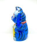 A hand-painted blue maneki-neko lucky cat figurine with black stripes, yellow eyes, pink inner ears, and a red collar, holding a yellow sign with black kanji characters, set against a plain white background.