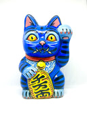 A hand-painted blue maneki-neko lucky cat figurine with black stripes, yellow eyes, pink inner ears, and a red collar, holding a yellow sign with black kanji characters, set against a plain white background.