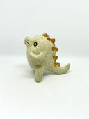 A small textured ceramic sculpture of a baby dinosaur with a light green-colored body, yellow eyes, and small gold spikes, standing against a plain white background.