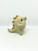 A small textured ceramic sculpture of a baby dinosaur with a light green-colored body, yellow eyes, and small gold spikes, standing against a plain white background.