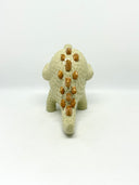 A small textured ceramic sculpture of a baby dinosaur with a light green-colored body, yellow eyes, and small gold spikes, standing against a plain white background.
