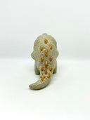 A small textured ceramic sculpture of a baby dinosaur with a light green-colored body, yellow eyes, and small gold spikes, standing against a plain white background.