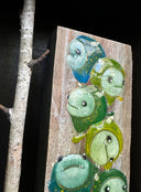 Open shadowbox artwork of a small yellow horned monster sculpt. It stands next to a vertical panel with many more monsters of the same kind painted on, mostly blue and greens. Birch branches are on either side.