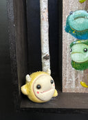 Close up of a small yellow horned monster character with a cute underbite smile. 