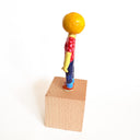 Figurine with a lemon head, wearing a red polka dot shirt and blue jeans on a wooden block with a white background