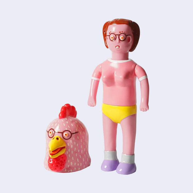 Vinyl figure of a pink skinned woman with glasses, short hair and buck teeth. She wears a pink top and yellow underwear. Next to her is a large chicken head, also with glasses.