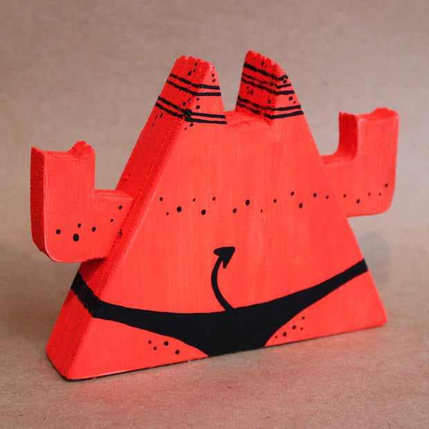 Wooden die cut sculpture of a red demon, shaped like a triangle with a very round belly. It wears only a black underwear and has its arms up at its side, making 2 "rock on" symbols.