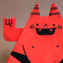 Wooden die cut sculpture of a red demon, shaped like a triangle with a very round belly. It wears only a black underwear and has its arms up at its side, making 2 "rock on" symbols.