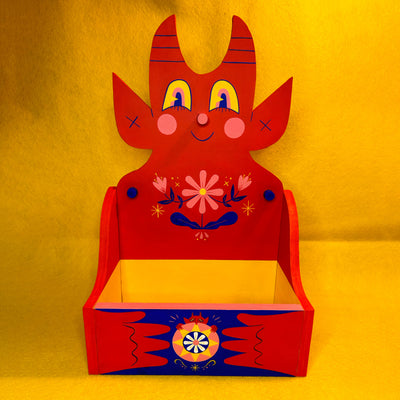 Wooden shelf with a large backing shaped like a cute, red devil with floral patterning on its chest.
