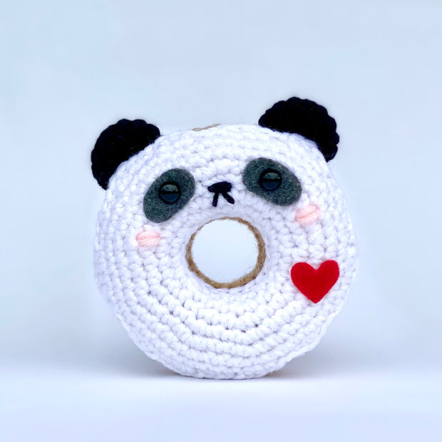 Crocheted donut fashioned like a panda bear. It has a cute smiling face and a red heart on its side.