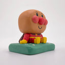 Wooden carving of a cute, round headed character with red cheeks and a nose sitting on a mound of grass.
