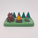 Camping-themed figure scene with a bear, campfire, and smiling rock with a mushroom growing atop it - all on a green base with trees and flowers.