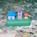 Small sculpture with a house, a purple bunny and a mushroom.