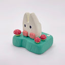Small wooden sculpture of a white Chibi Totoro sitting on a green base with tiny mushroom around.