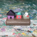 Small sculpture with a house, an eyeball character and a skull on a rock