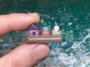 Small sculpture with a house, an eyeball character and a skull on a rock