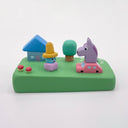 Colorful clay model of a scene with a house, trees, and a purple horse riding in a tiny pink car.