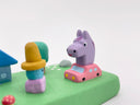 Colorful clay model of a scene with a house, trees, and a purple horse riding in a tiny pink car.
