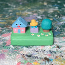 Small sculpture with a house, a blue guy with a hat, and a tree.