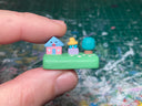 Small sculpture with a house, a blue guy with a hat, and a tree.