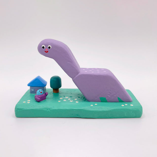 Purple dinosaur-like creature with a small house and tree on a green base against a white background