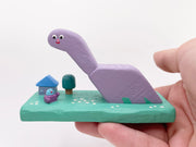 Purple dinosaur-like creature with a small house and tree on a green base against a white background