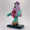 Sculpture of a triangular folklore character with one eye, a nose, its tongue sticking out of its mouth and standing on one leg, which wears a wooden sandal.