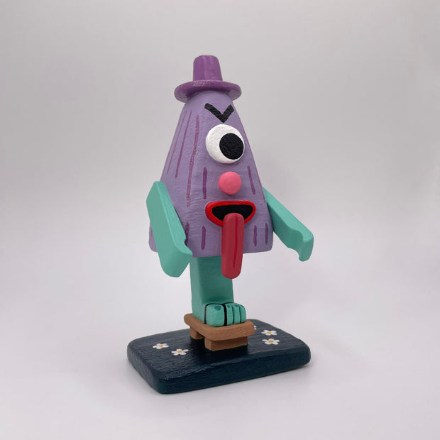 Sculpture of a triangular folklore character with one eye, a nose, its tongue sticking out of its mouth and standing on one leg, which wears a wooden sandal.