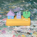 Small sculpture with a house, a purple frog and a cactus.