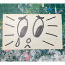 Ink drawing of a cartoon face on an index card.