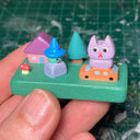 Colorfully painted small wooden sculpture with various elements of a witch character, a cat atop a tiny car, a house, tree and tiny mushroom.
