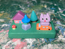 Colorfully painted small wooden sculpture with various elements of a witch character, a cat atop a tiny car, a house, tree and tiny mushroom.