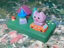 Colorfully painted small wooden sculpture with various elements of a witch character, a cat atop a tiny car, a house, tree and tiny mushroom.