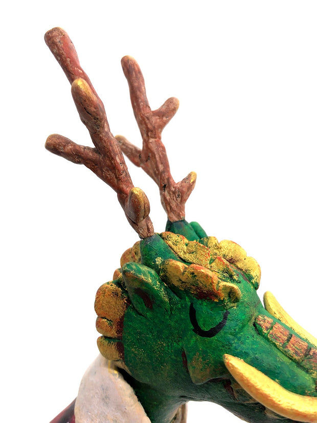 Sculpture of a green dragon with wooden antlers and yellow/gold color accents. It stands on 2 legs like a human and wears a red sherpa flannel jacket.