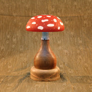 Carved wooden mushroom, with a thick and smooth wooden base. The top of the mushroom is red with while polka dots. Sculpture is also a lamp, emitting a dim glow.