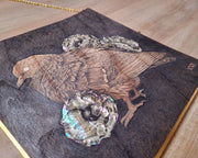 Close up view of a wood panel with an inlayed wood design of a bird and flowers made of abalone flowers.
